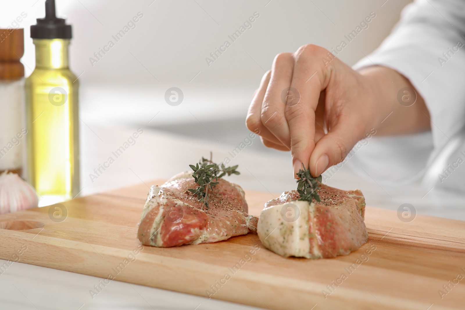 Photo of Professional chef decorating delicious meat with thyme at white table, closeup