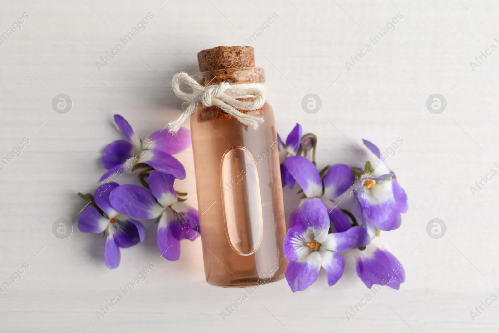 Photo of Beautiful wild violets and essential oil on white wooden table, flat lay. Spring flowers