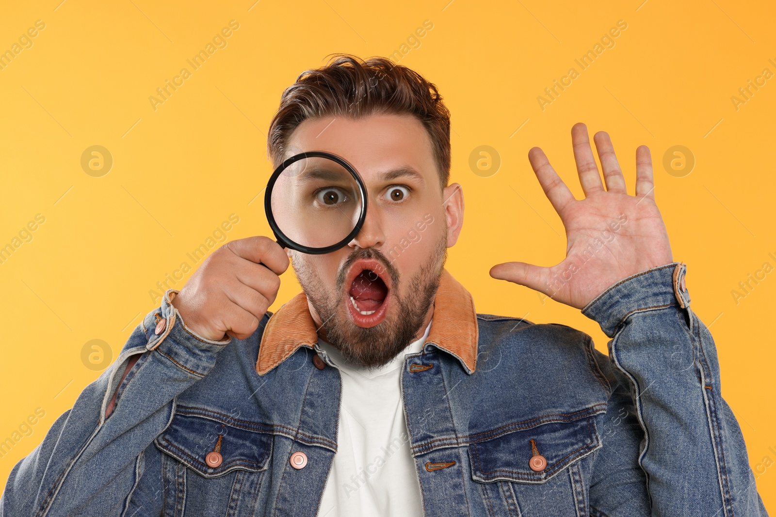 Photo of Emotional man looking through magnifier on yellow background