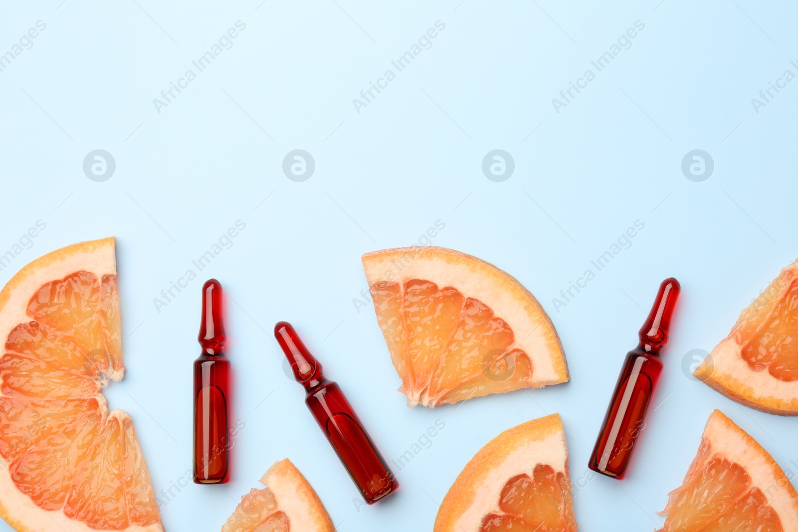 Photo of Skincare ampoules with vitamin C and slices of grapefruit on light blue background, flat lay. Space for text