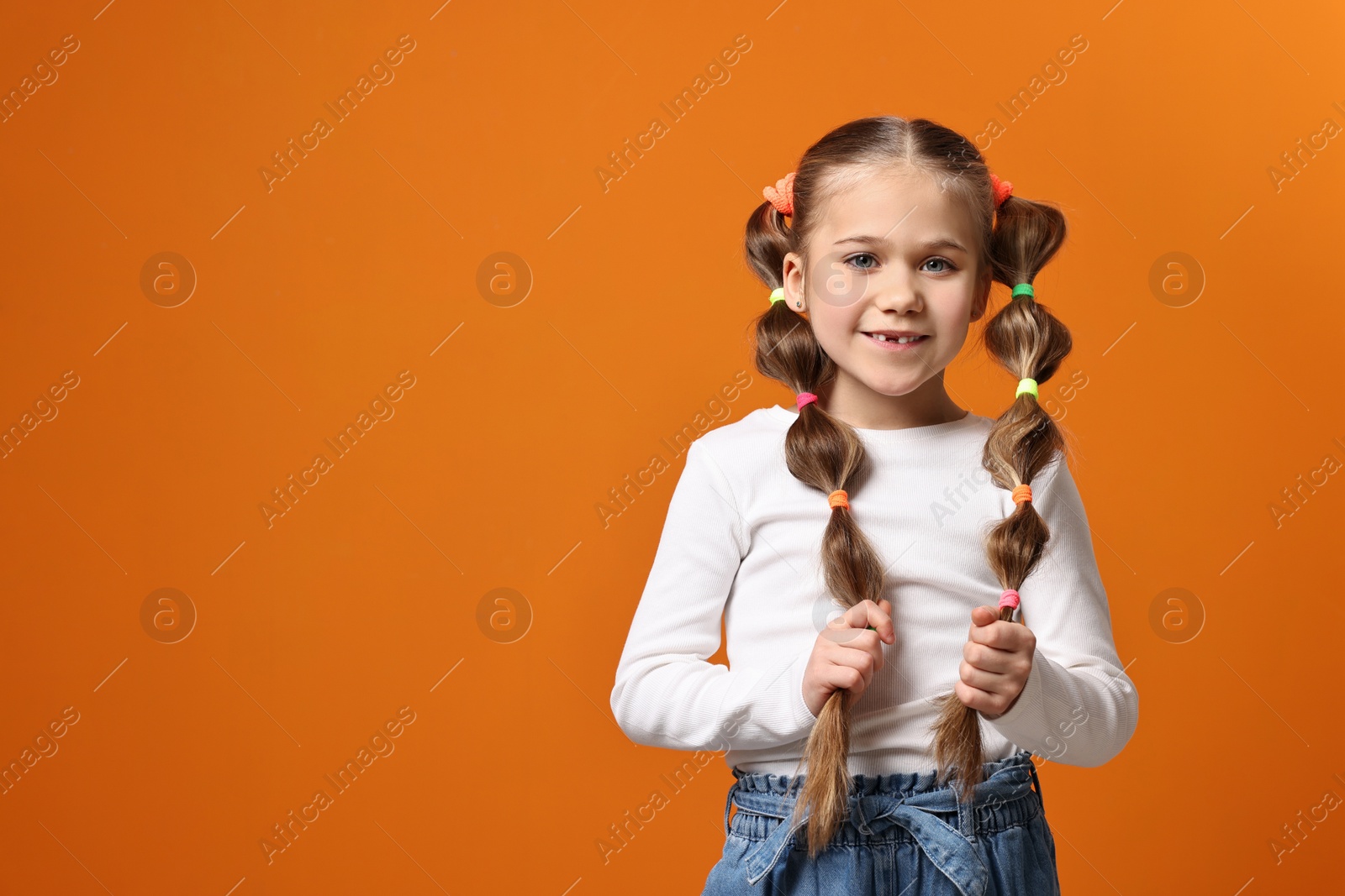 Photo of Cute little girl with beautiful hairstyle on orange background. Space for text