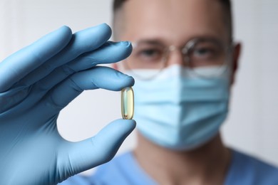 Photo of Doctor holding pill on light background, selective focus. Space for text