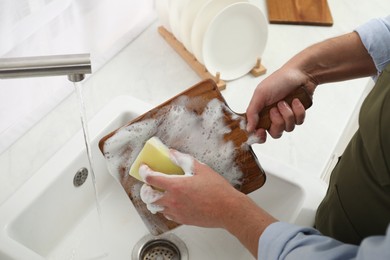 Man washing wooden cutting board in kitchen, closeup
