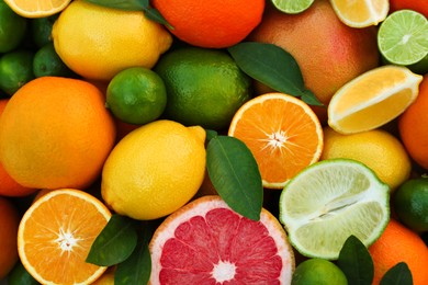 Photo of Different fresh citrus fruits and leaves as background, top view.