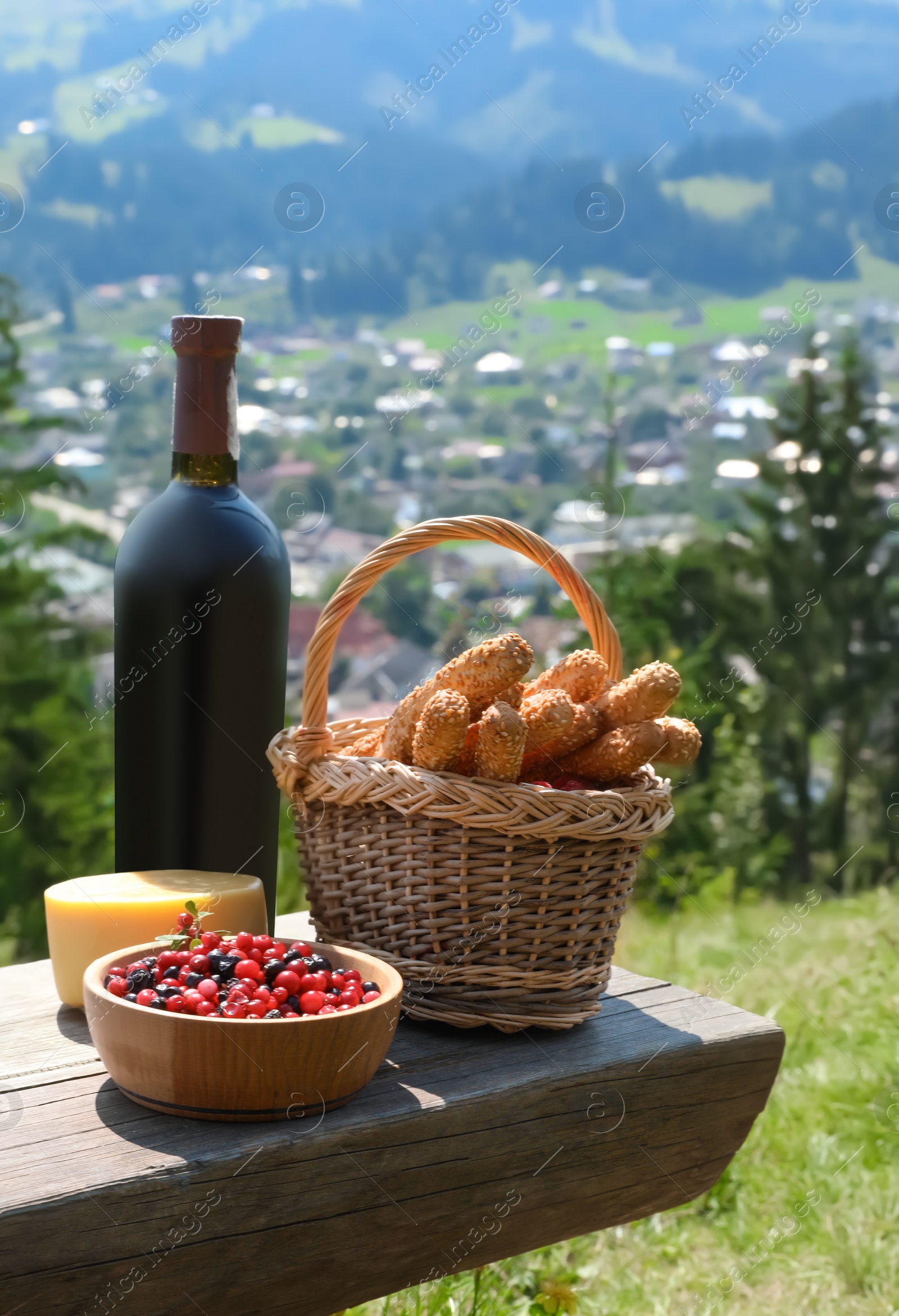 Photo of Bottle of red wine and food for picnic on bench against mountain landscape