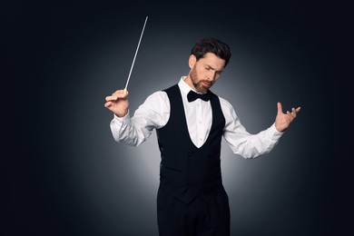 Professional conductor with baton on dark background