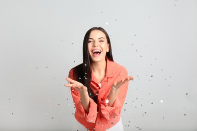 Photo of Emotional woman and falling confetti on light grey background
