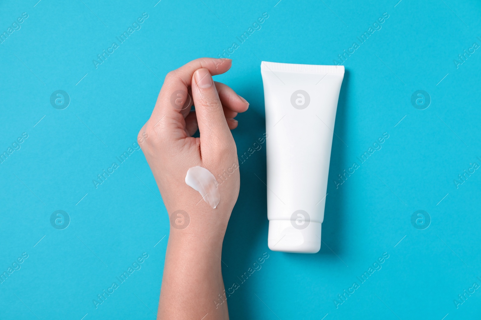 Photo of Woman with tube of hand cream on light blue background, top view