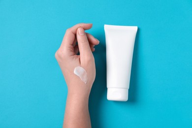 Woman with tube of hand cream on light blue background, top view