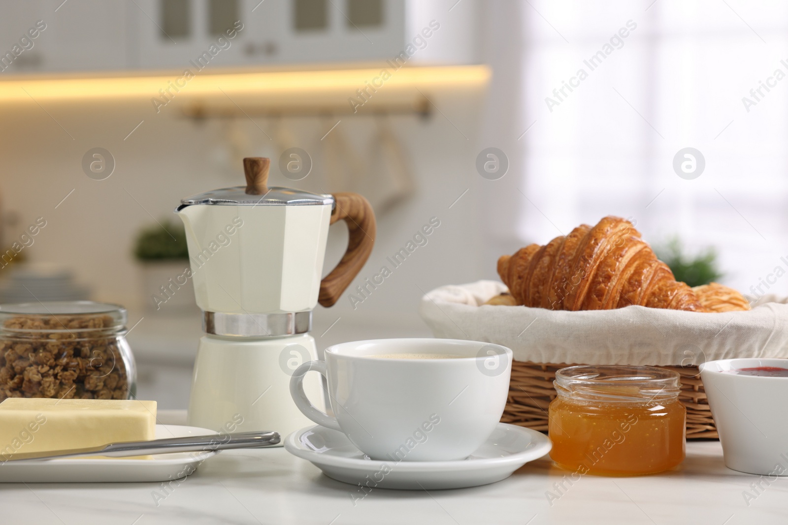 Photo of Breakfast served in kitchen. Fresh coffee, granola, croissants, jam, butter and honey on white table