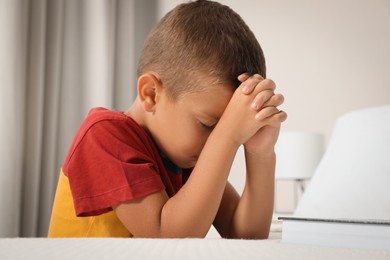 Photo of Cute little boy with hands clasped together saying bedtime prayer at home