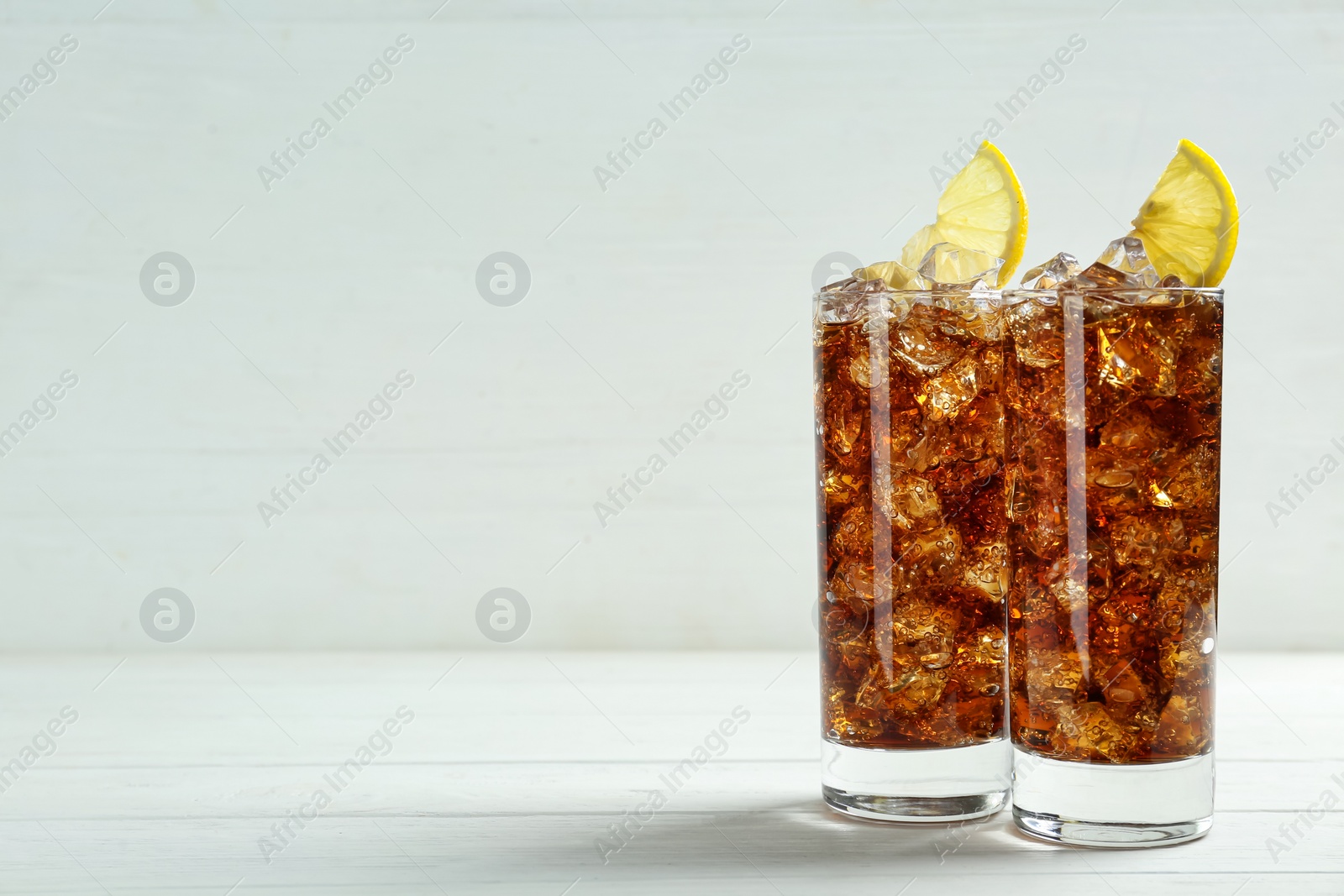 Photo of Glasses of refreshing soda water with ice cubes and lemon slices on white wooden table, space for text