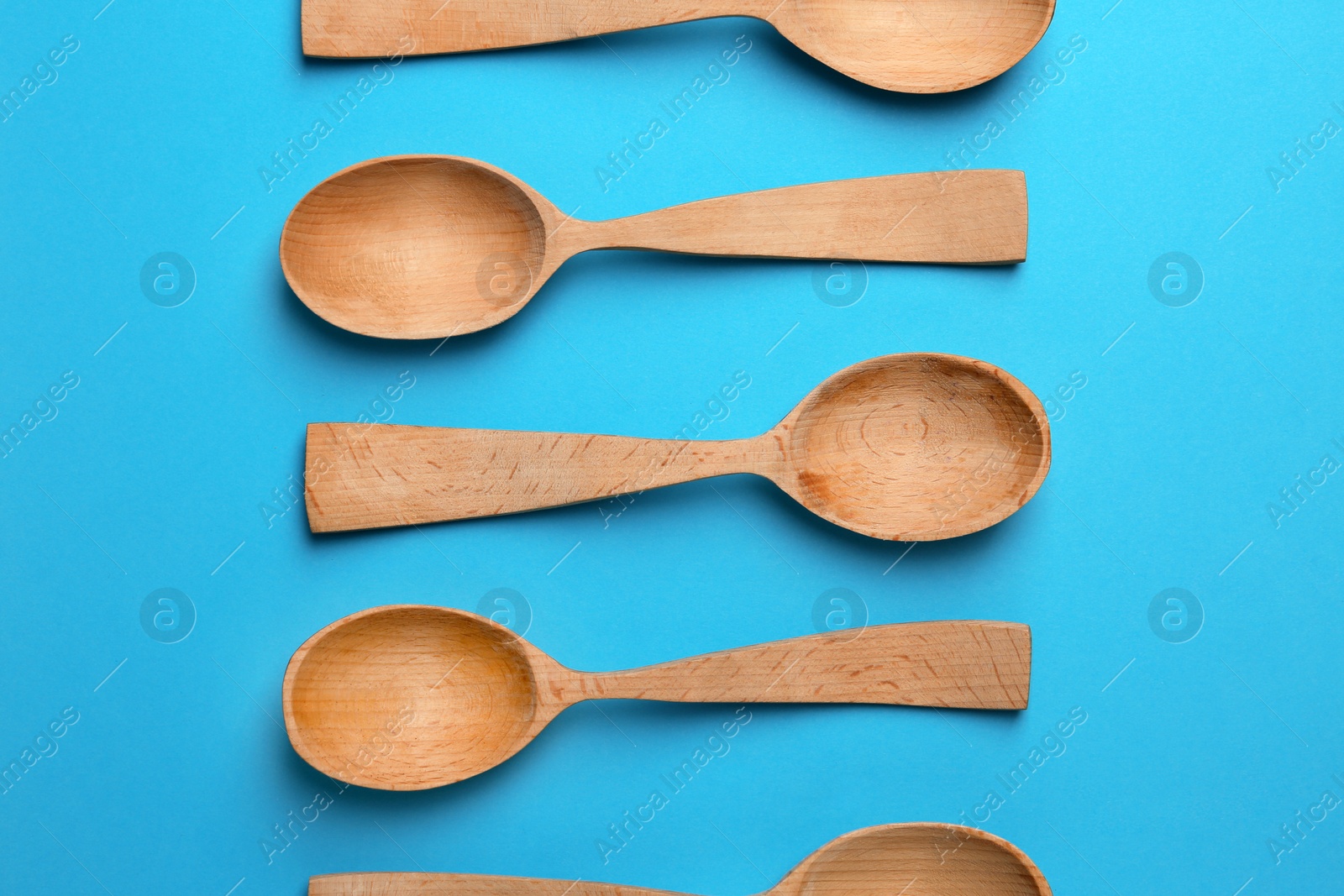 Photo of Clean empty wooden spoons on blue background, flat lay