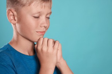 Photo of Boy with clasped hands praying on turquoise background, closeup. Space for text