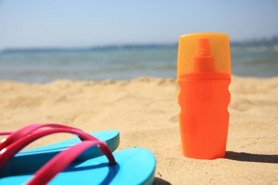 Sunscreen and flip flops on sandy beach. Sun protection care