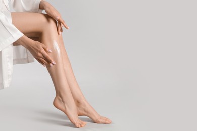 Photo of Woman applying body cream onto her smooth legs on light grey background, closeup. Space for text