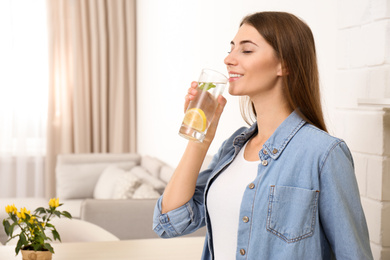 Young woman drinking lemon water in kitchen. Space for text