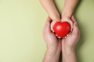 Father and his child holding red decorative heart on light green background, top view. Space for text