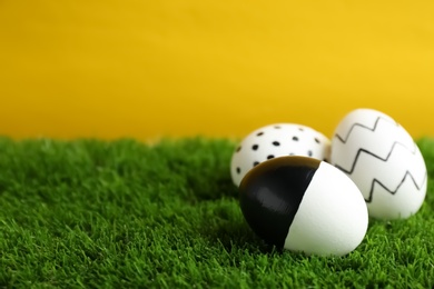 Traditional painted Easter eggs on green lawn against color background, space for text