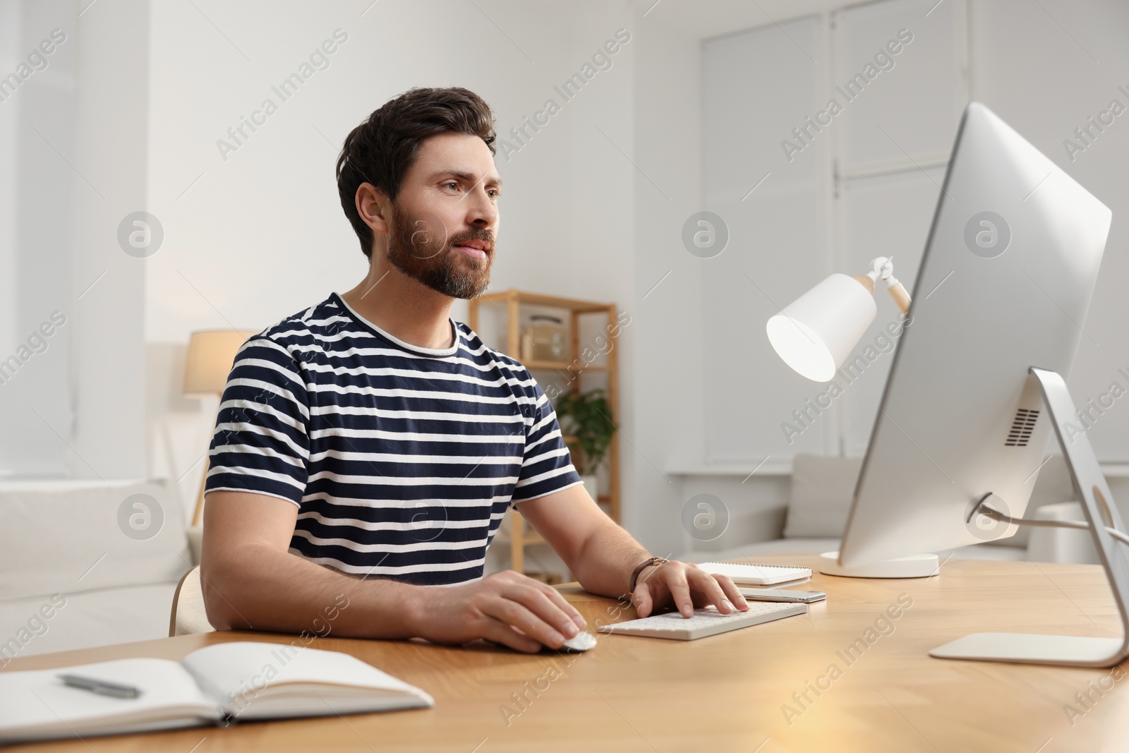 Photo of Home workplace. Man working with computer at wooden desk in room