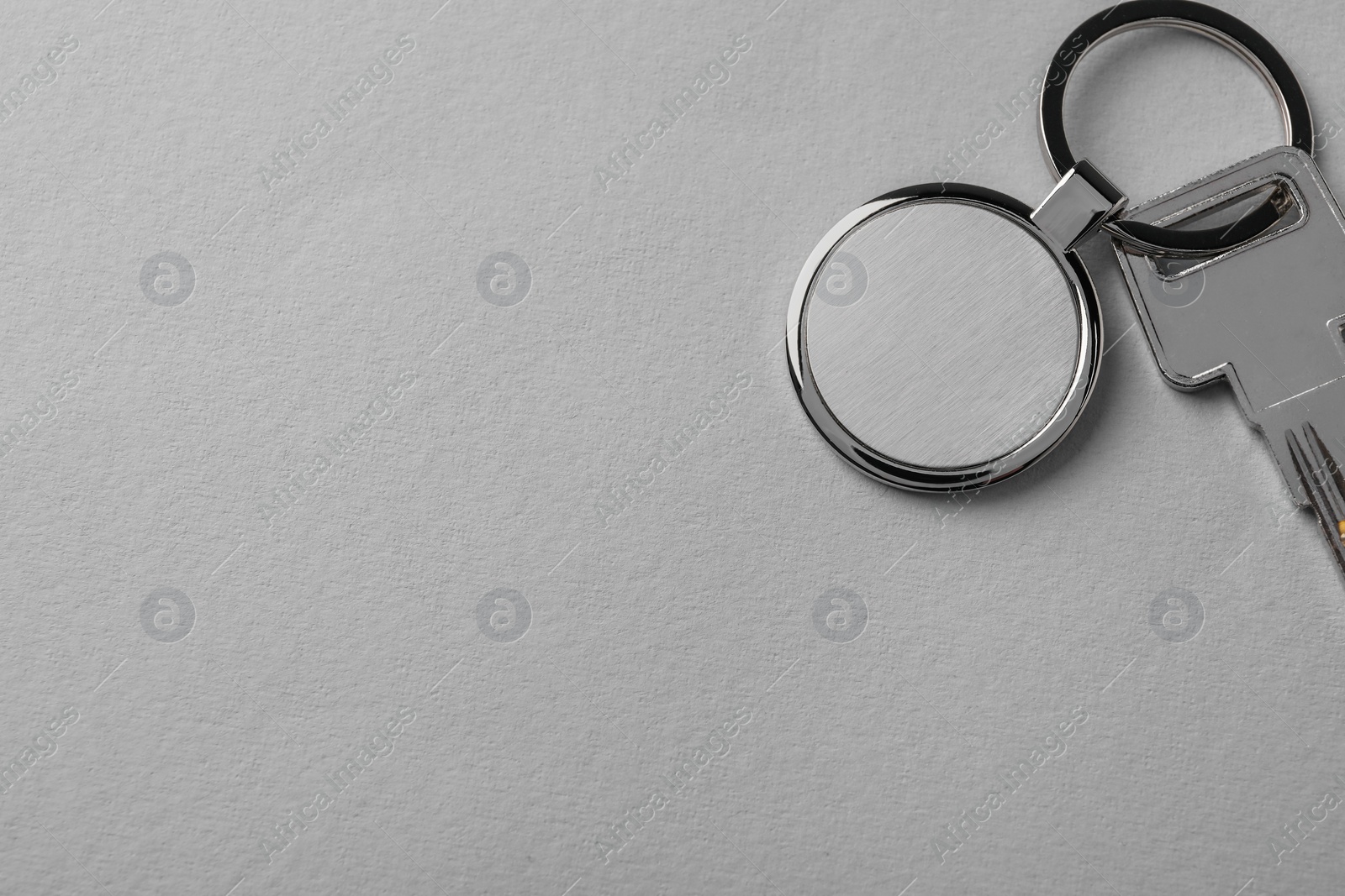 Photo of Key with metallic keychain on light grey background, top view. Space for text
