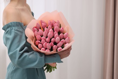 Photo of Woman holding bouquet of pink tulips indoors, closeup. Space for text
