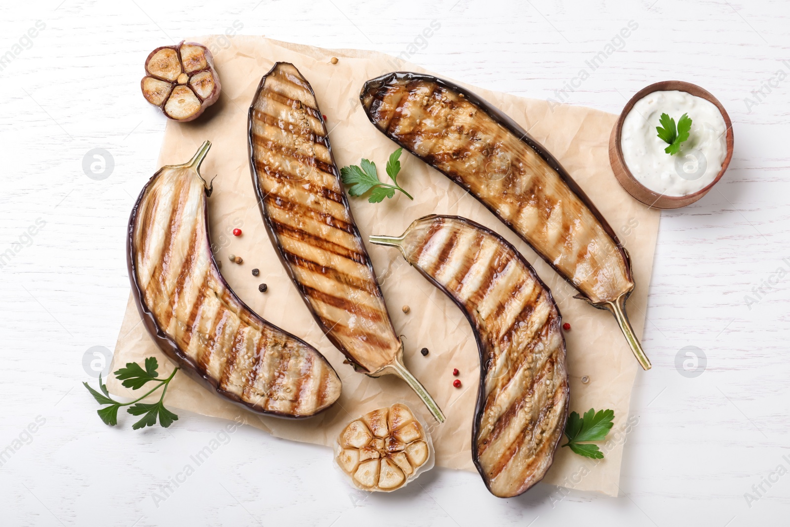 Photo of Delicious grilled eggplant halves and sauce on white wooden table, flat lay