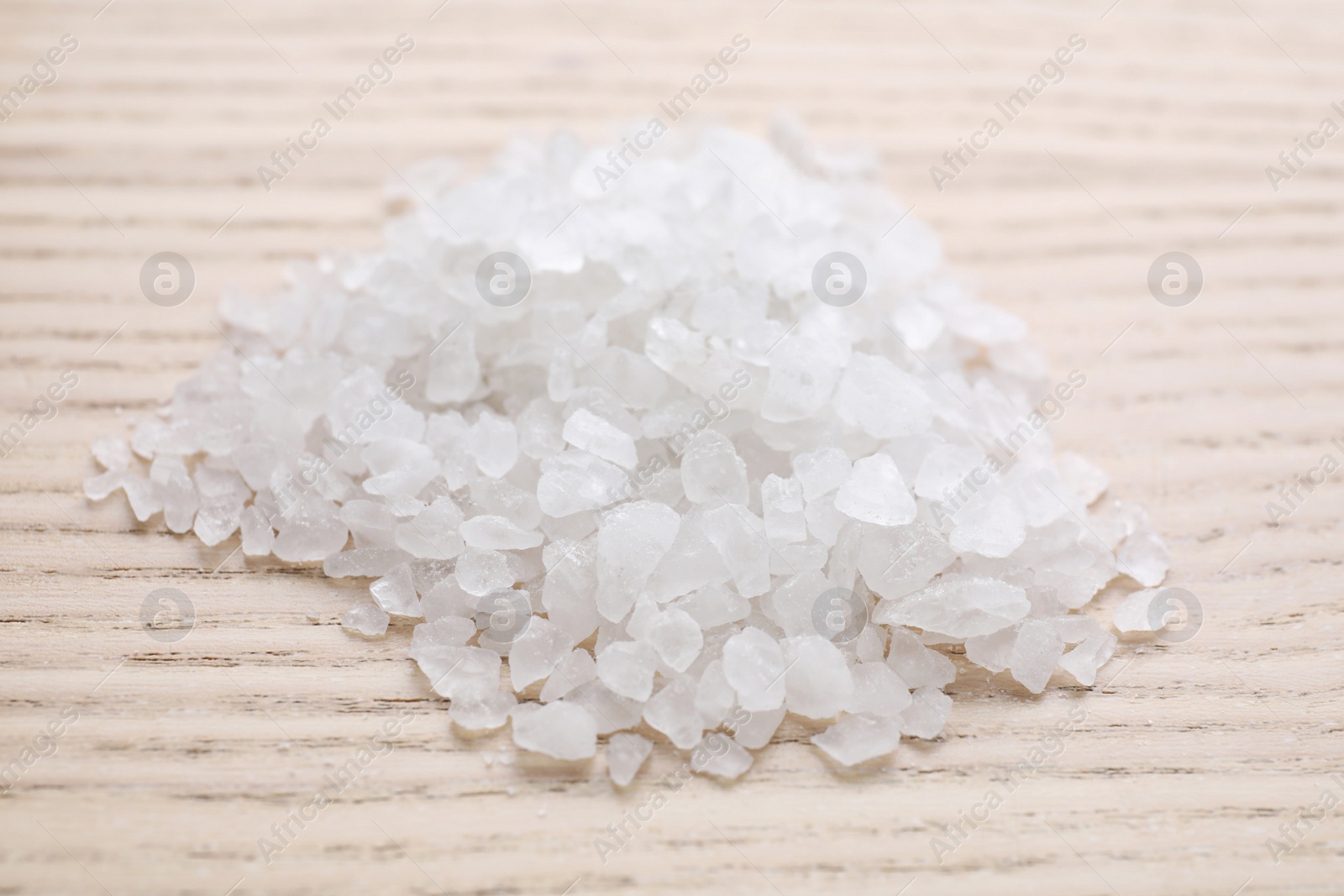 Photo of Pile of white sea salt on wooden table, closeup. Spa treatment