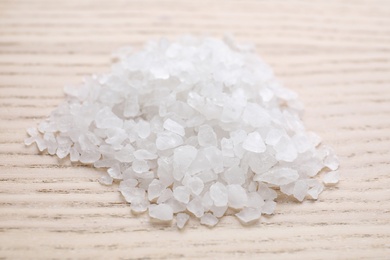 Photo of Pile of white sea salt on wooden table, closeup. Spa treatment