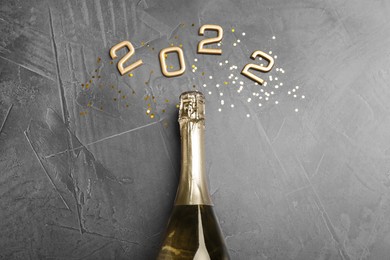 Photo of Bottle of sparkling wine, gold confetti and number 2022 on grey background, flat lay. Happy New Year