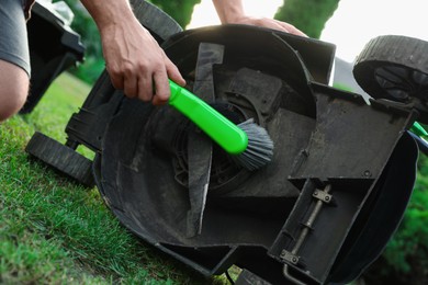 Man cleaning lawn mower with brush in garden, closeup