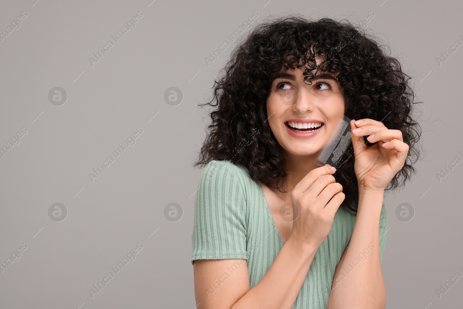 Photo of Young woman holding teeth whitening strips on grey background, space for text