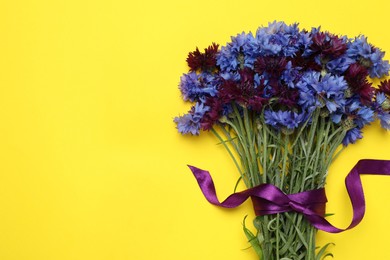 Photo of Bouquet of beautiful colorful cornflowers on yellow background, top view. Space for text