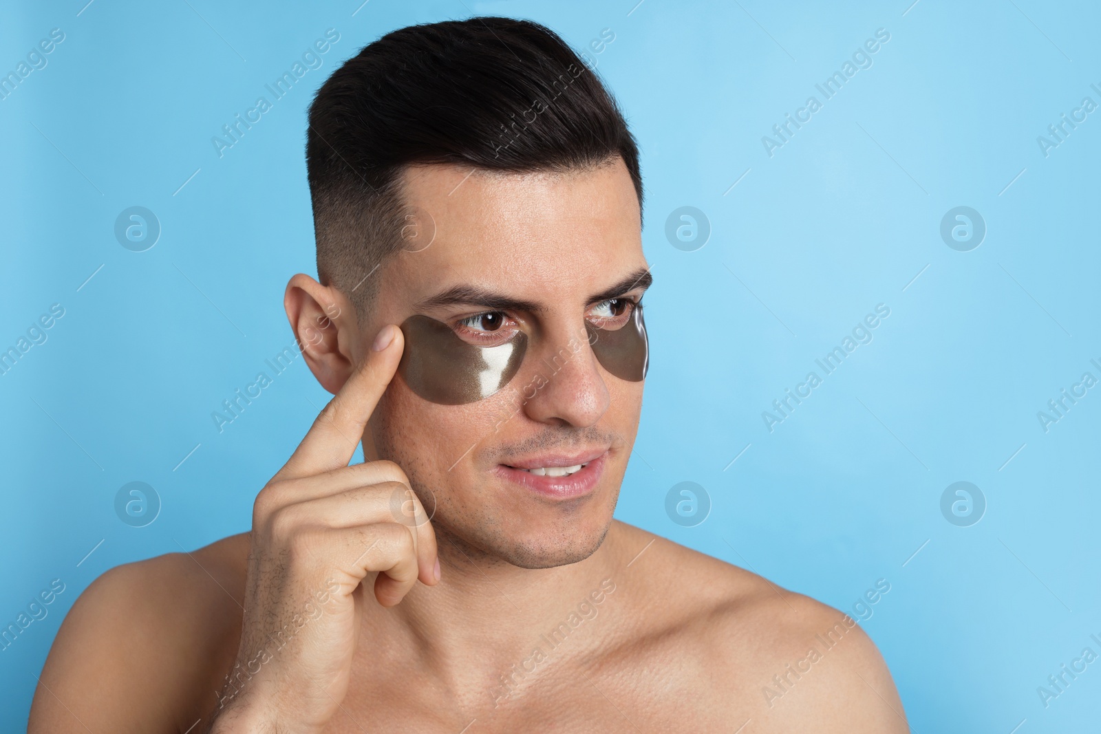 Photo of Man applying dark under eye patch on light blue background. Space for text