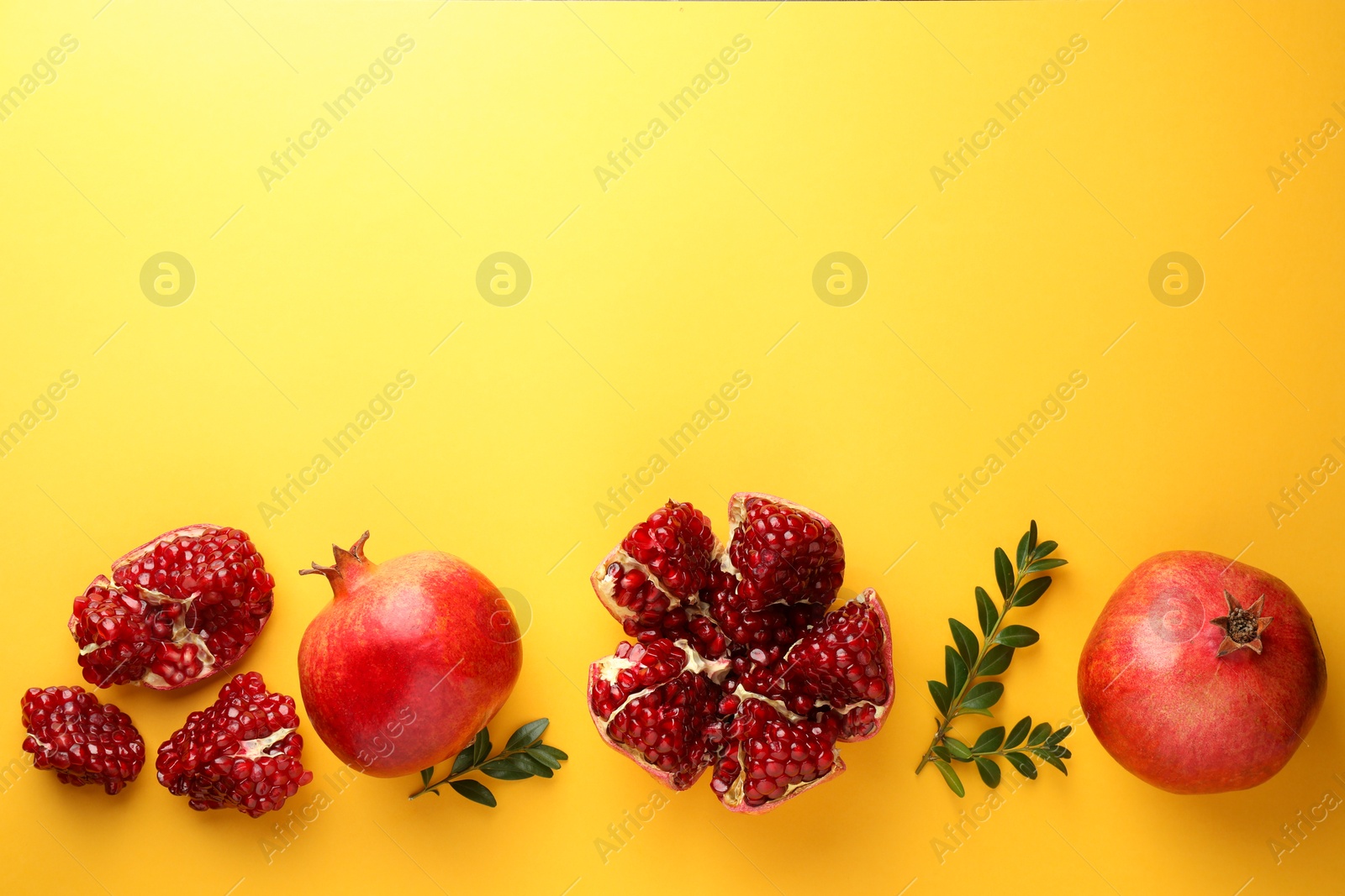 Photo of Fresh pomegranates and green leaves on yellow background, flat lay. Space for text