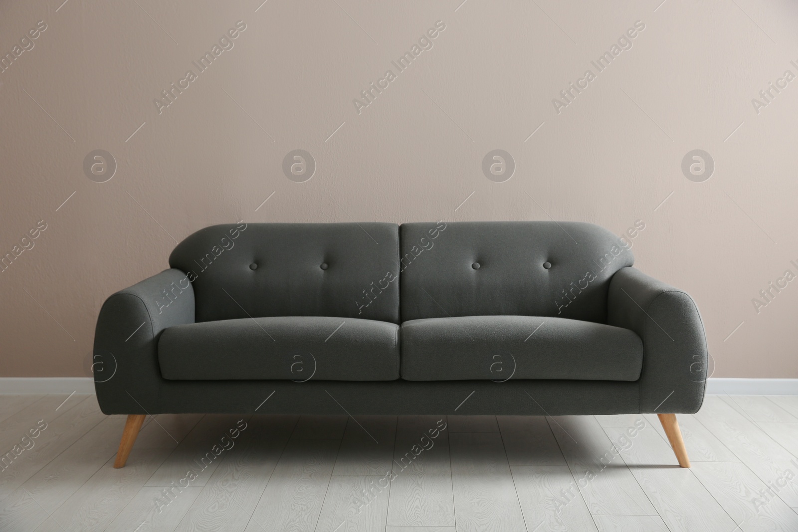 Photo of Comfortable grey sofa near beige wall indoors. Interior design