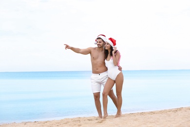 Happy young couple with Santa hats on beach near sea