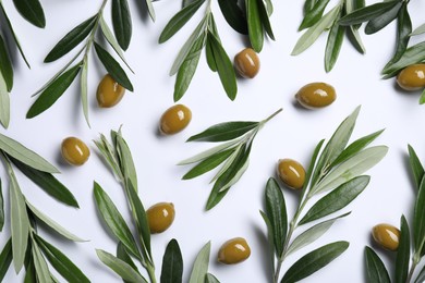 Twigs with olives and fresh green leaves on white background, flat lay