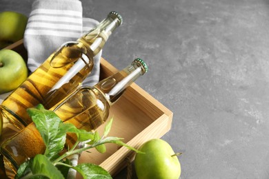 Photo of Delicious cider, ripe apples and green leaves on gray table, closeup. Space for text