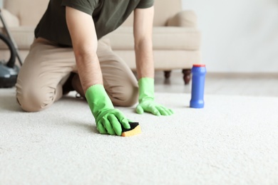 Photo of Young man cleaning carpet at home