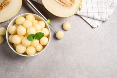 Photo of Melon balls and mint in bowl on light grey table, flat lay. Space for text