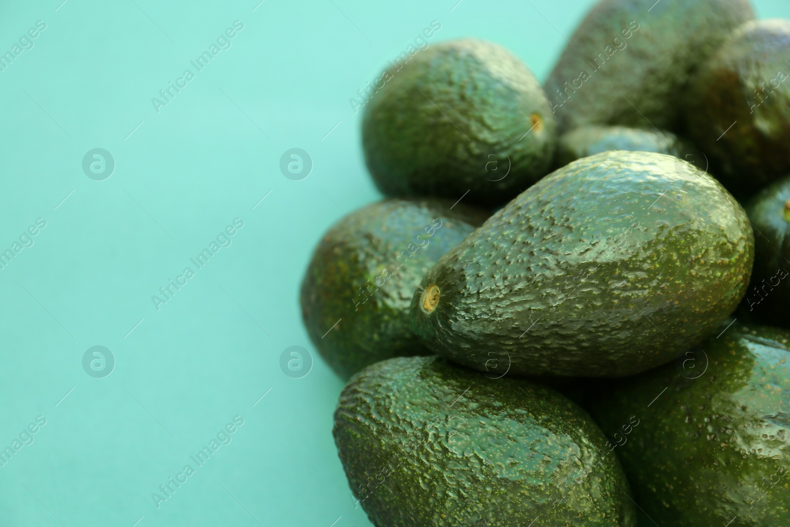 Photo of Many tasty ripe avocados on turquoise background. Space for text