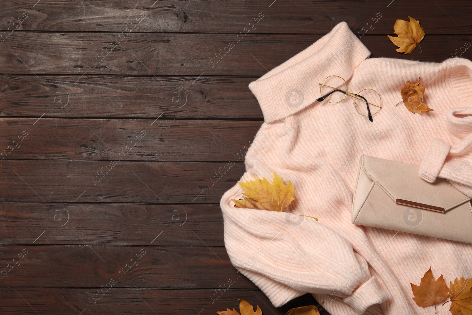 Photo of Warm sweater, bag and dry leaves on brown wooden background, flat lay with space for text. Autumn season