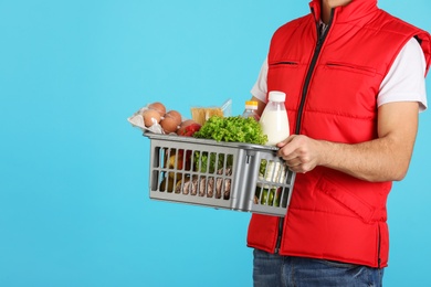 Photo of Man holding basket with fresh products on color background, closeup. Food delivery service