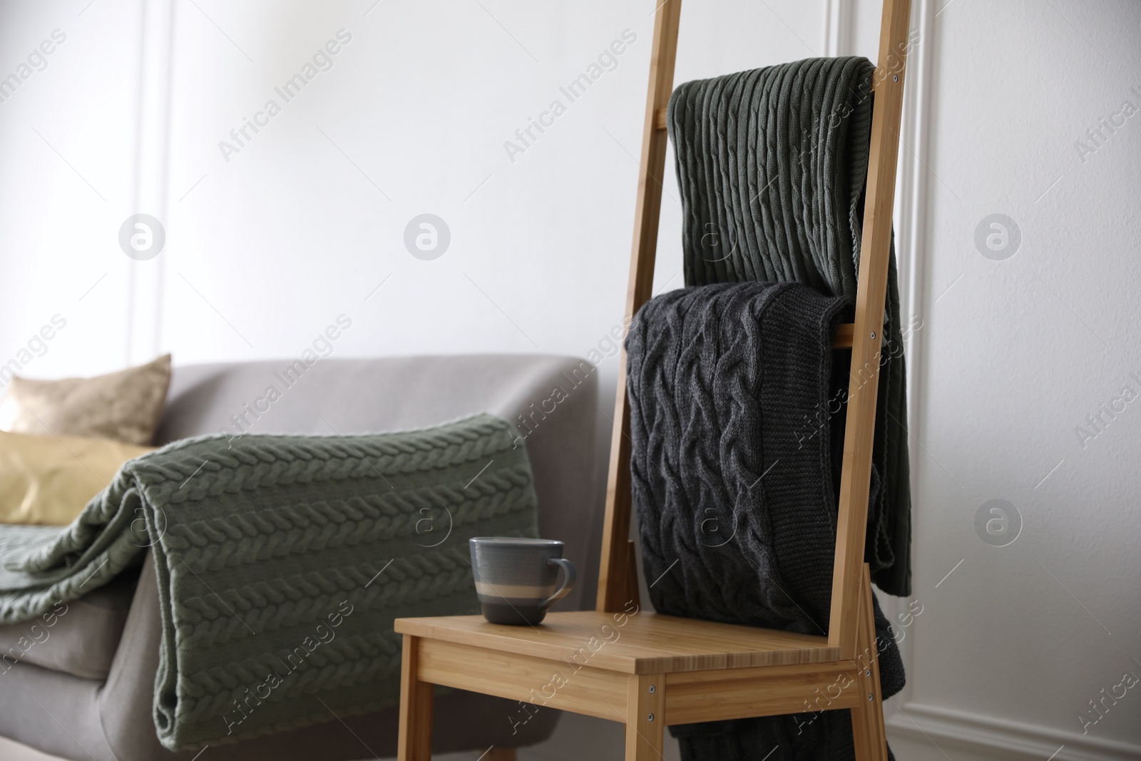 Photo of Knitted plaids on chair near sofa in living room