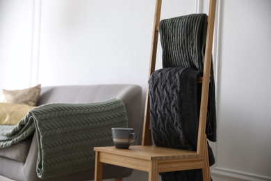 Photo of Knitted plaids on chair near sofa in living room