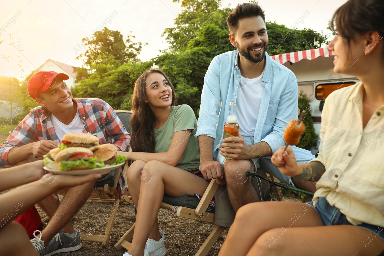 Photo of Happy friends with food and beer resting near motorhome. Camping season