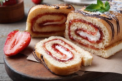 Photo of Tasty cake roll with strawberry jam and cream on wooden table, closeup