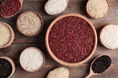 Photo of Flat lay composition with brown and other types of rice in bowls and spoons on wooden table