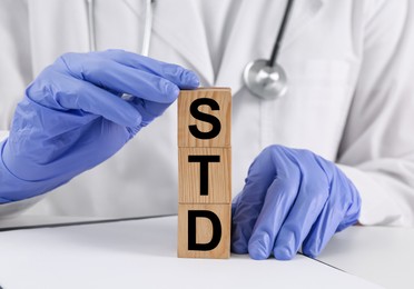 Doctor and wooden cubes with abbreviation STD at white table, closeup